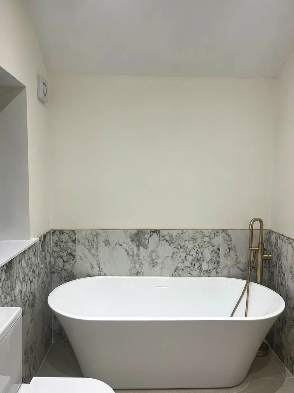 Freestanding bath with floor-mounted tap and marble-effect half-height tiling in the Bramhall bathroom